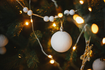 Modern christmas tree ornaments, white baubles and golden christmas lights bokeh close up. Space for text. Atmospheric festive decorated scandinavian room. Stylish christmas decor