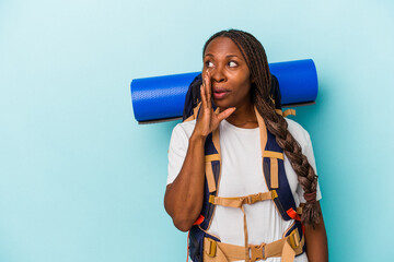 Young african american hiker woman isolated on blue background is saying a secret hot braking news and looking aside