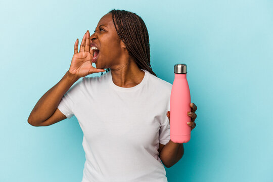 Young african american woman holding canteen isolated on blue background shouting and holding palm near opened mouth. - Powered by Adobe