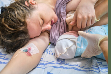 The first breast feeding of a newborn baby boy immediately after giving birth on a hospital bed in a maternity ward - Powered by Adobe