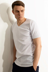 Young confident sexual athletic man with brown hair. Man dressed in white T-shirt and standing near white wall.