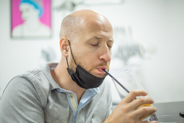 Caucasian male with mask and closed eyes is drinking his long drink with a straw