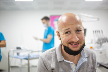 Scared caucasian male with mask in a dental clinic is waiting for a teeth check up. Nurse and dental care equipment on the background