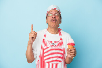 Senior american ice cream man holding an ice cream isolated on blue background pointing upside with opened mouth.