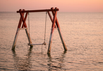 wooden swing in the water at sunset