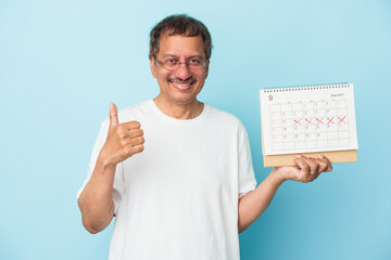 Senior indian man holding a calendar isolated on blue background smiling and raising thumb up