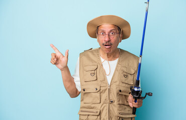 Senior indian fisherman holding rod isolated on blue background pointing to the side