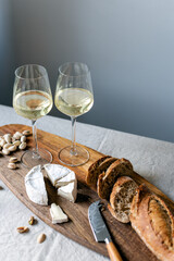 Two glasses of white wine and a wooden board with appetizers on the table.