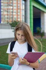 Cute schoolgirl on the street with a smartphone, notebooks, and a backpack. Back to school. Concept education