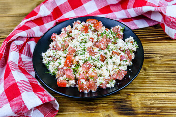 Salad with tomatoes, cottage cheese, dill and olive oil on a wooden table