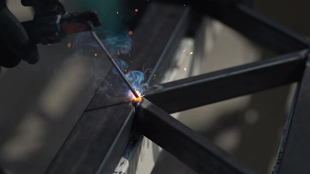 Employee man welding steel with sparks using mig mag welder, sparks flying around from the welding metal, closeup