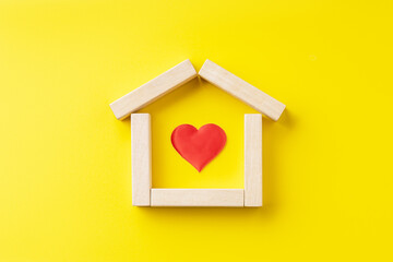 house shape made by wooden blocks with red heart inside over yellow background. outer space. real...