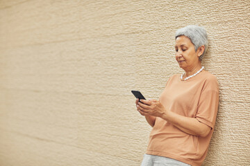 Minimal side view portrait of modern mature woman using smartphone while standing against yellow wall outdoors, copy space