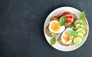two toast breads with vegetables, egg and basil on a plate on a black concrete table