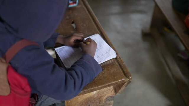 Black poor African kid doing homework, writing in his notebook at school. Africa 4K.
