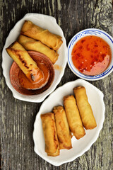 crispy egg rolls on small white platters with little bowls of dipping sauces on rustic wood tabletop - 451308227