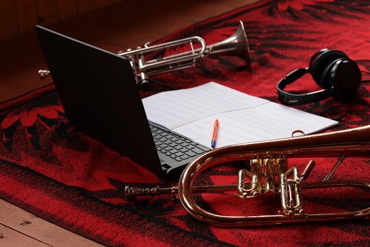 Musical theme and attributes close up. Laptop headphones notes with pen musical instruments golden flugelhorn and trumpet lying on the floor on a red background creativity and entertainment
