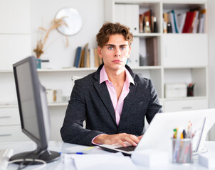 Focused attractive young man working with laptop and documents in office