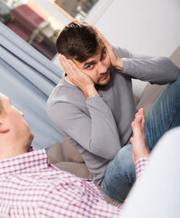 Upset man having unpleasant talk with male colleague on couch in home interior