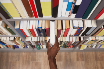 Top view close up of male hand taking book off shelf in library, copy space