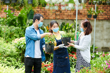 Customers in medical masks asking gardening center worker to help them with choosing flowers