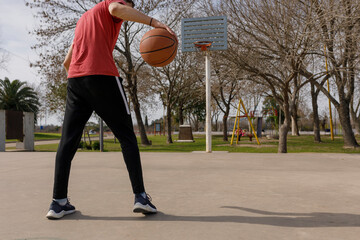 young basketball player pokes the ball on the ground while looking at the basket. Court in a park....