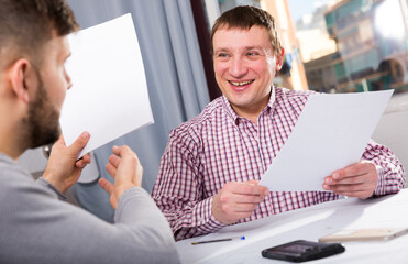 Satisfied man with male partner working with documents sitting at table at home