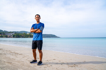 Fototapeta na wymiar Healthy Asian man in sportswear jogging or running on the beach by the sea in summer morning. Strong athlete male do sport training workout fitness on the beach with listen to music from smartphone