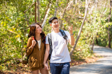 Smiling young Asian couple holding hands hiking and climbing together in forest. Happy man with girlfriend relax and enjoy summer outdoor lifestyle with beautiful nature on holiday vacation travel.