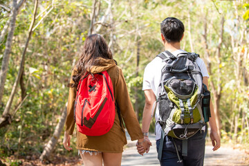 Smiling young Asian couple holding hands hiking and climbing together in forest. Happy man with girlfriend relax and enjoy summer outdoor lifestyle with beautiful nature on holiday vacation travel.