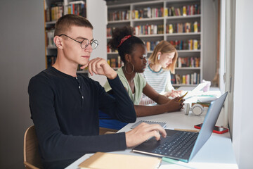 Fototapeta na wymiar Side view portrait of three students sitting in row at desk while studying in school library, copy space