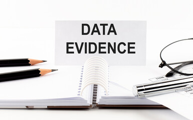 Text DATA EVIDENCE on paper card,pen, pencils, glasses,financial documentation on table - business concept
