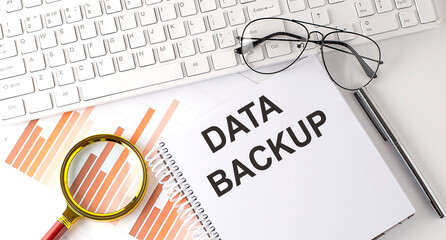 DATA BACKUP text written on a notebook with keyboard, chart,and glasses