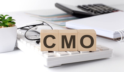 Fototapeta premium CMO Chief Marketing Officer written on a wooden cube on keyboard with office tools