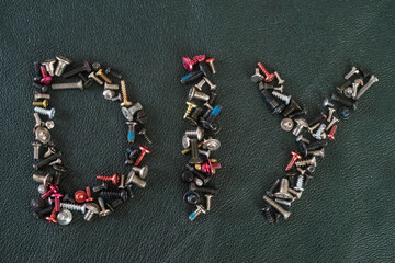DIY written with tiny metal screws on black leather texture, macro