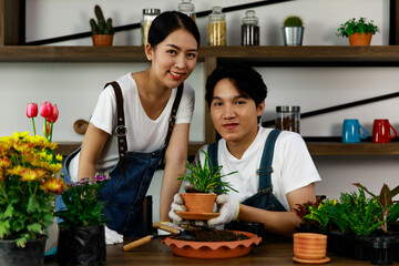 Young asian couple wearing jean overall and white t-shirt doing gardening and growing small plants and trees. Concept home garden hobby