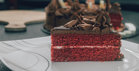 Chocolate cake slice on a white ceramic plate on the tabletop. Icing flowers and chocolate pieces as toppings. Delicious Icing Birthday cake design side close-up view.