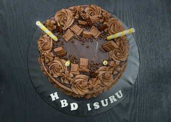 Round chocolate cake design. Delicious sweet food for birthday event. chocolate pieces and icing flower toppings. Cake on top of black table, directly overhead view.