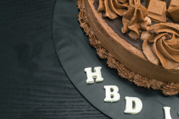 Round chocolate cake design. Delicious sweet food for a birthday event. chocolate pieces and icing flower toppings. Cake on top of black table, copy space for text on the left.