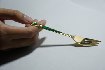 a hand holding a golden fork, on a white background