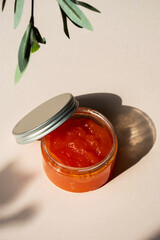 Jar of organic skin care mandarin gel. Package of cosmetic product body cream in sunlight with shadows of olive branches. SPA treatment or beauty industry concept.