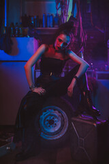Fototapeta na wymiar girl in a cyberpunk suit with a neon light in the garage. Steampunk cosplay in the post-apocalyptic style
