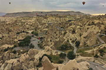 Amazing landscape of Cappadocia, view from a height. There are many rocks with bizarre outlines and caves. A mountain with a flat top on the horizon. Colorful balloons are flying in the dawn sky