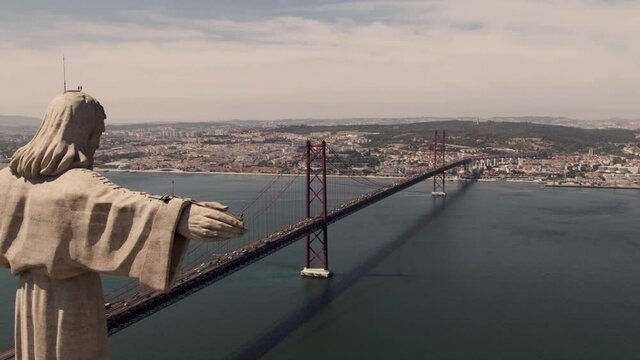 Open arms Cristo Rey overlooking Lisbon cityscape and 25 de Abril Bridge over tagus river.