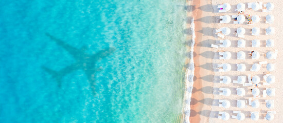 Stunning aerial view of white beach umbrellas on a white sand beach bathed by a turquoise water and the shadow of an airplane landing in Sardinia. Liscia Ruja,Sardinia, Italy. © Travel Wild