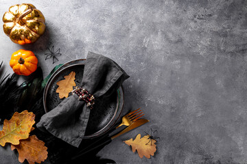 Halloween table setting concept. Plate, golden cutlery, pumpkins, spooky Halloween decorations and autumn leaves on gray background, photo with free space for text