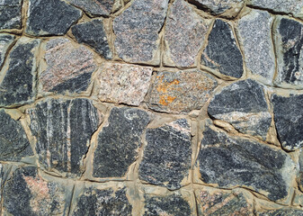 The masonry wall is made of large natural dark granite blocks. Stone background.