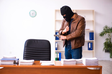 Young man in balaclava stealing information from the office