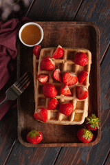 Fototapeta na wymiar Fresh homemade Belgian waffles on an old wooden table with strawberries and honey.