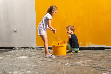 A boy and a girl paints a wall at home in yellow